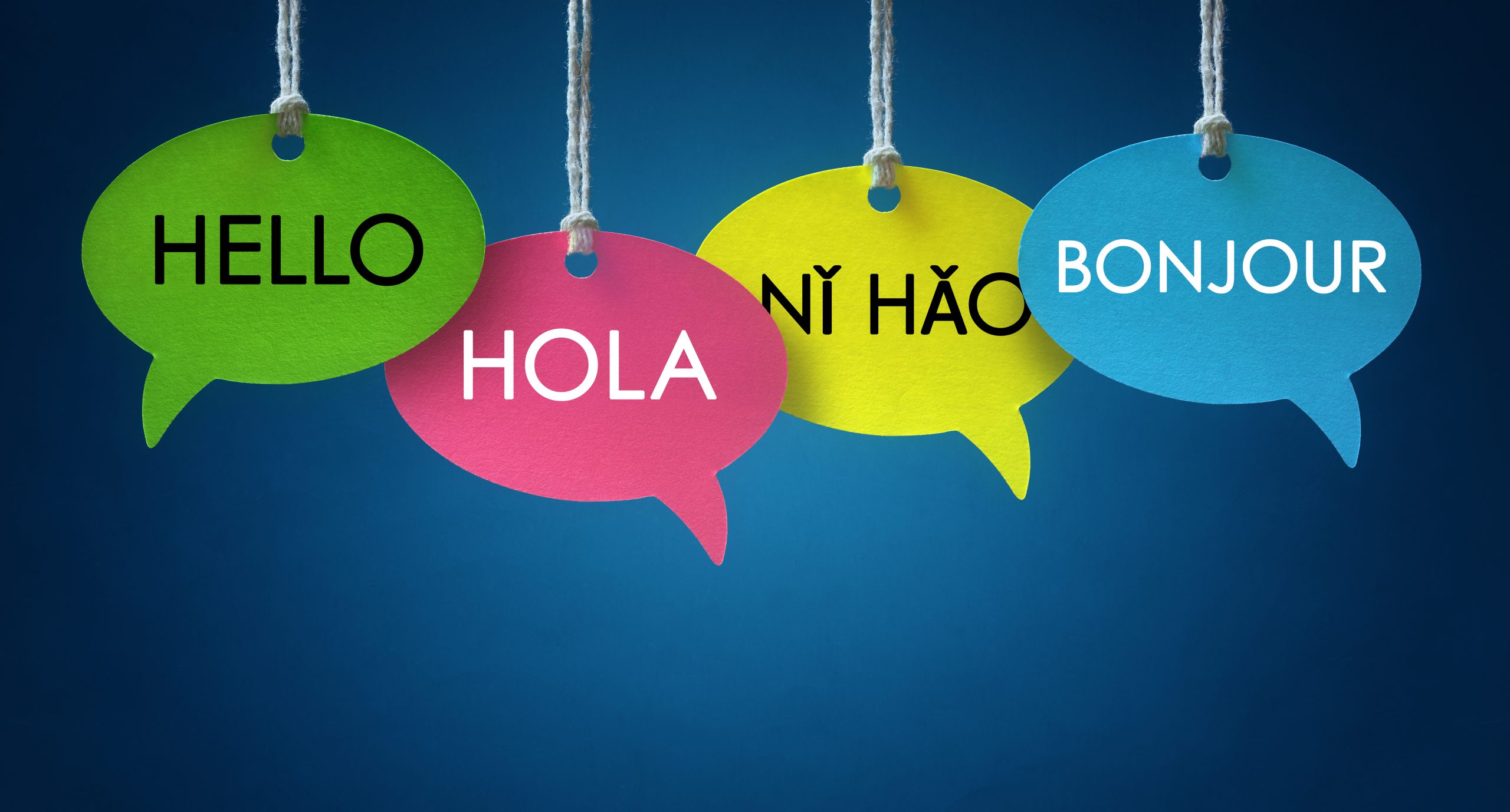 Foreign language colorful communication speech bubbles hanging from a cord over blue background
